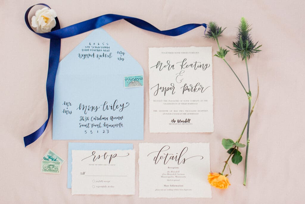 Wedding invitation suite flat lay with blue envelope and thistle at The Blaisdell, Minneapolis