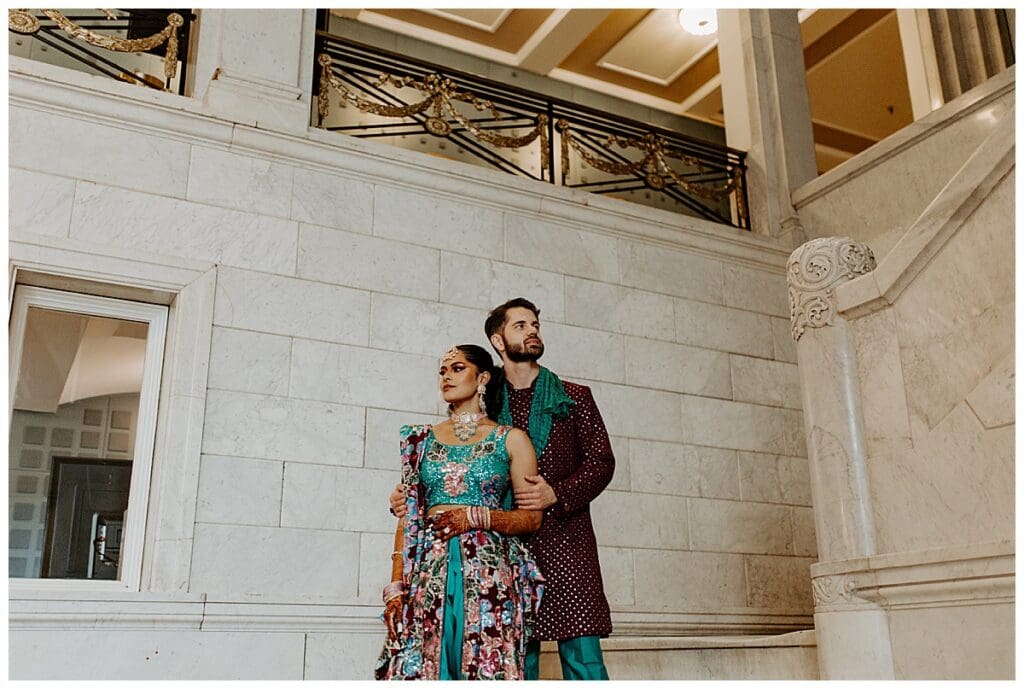 Aarushi and Shane standing together on the steps inside the Lumber Exchange in downtown Minneapolis during their Indian wedding weekend