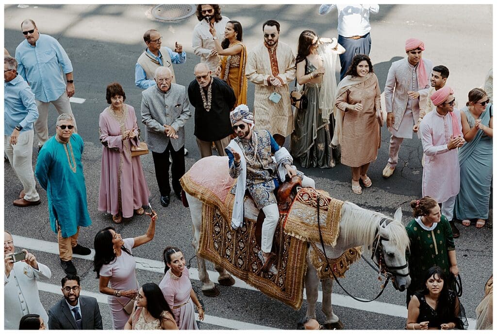 Shane on a white horse during the traditional baraat procession at their Minneapolis Indian wedding at Mosaic Venue