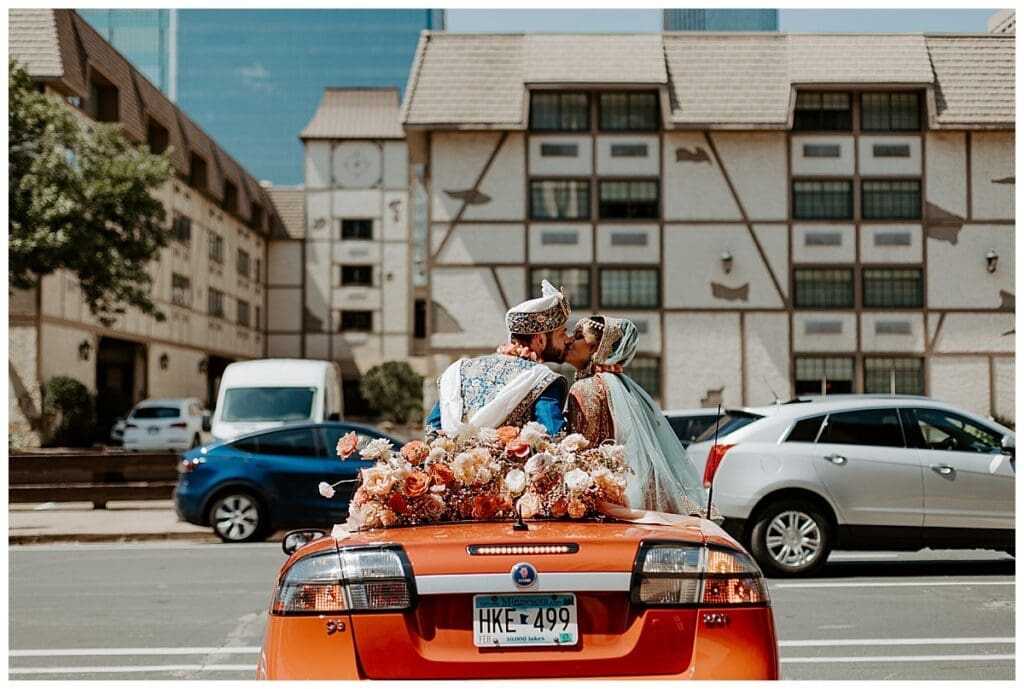 Aarushi and Shane share a kiss in a decorated red convertible during the baraat at their Minneapolis Indian wedding at Mosaic Venue