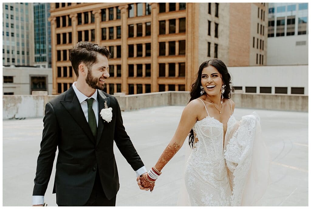 Aarushi and Shane walking hand in hand on the rooftop of the Lumber Exchange with the Minneapolis skyline