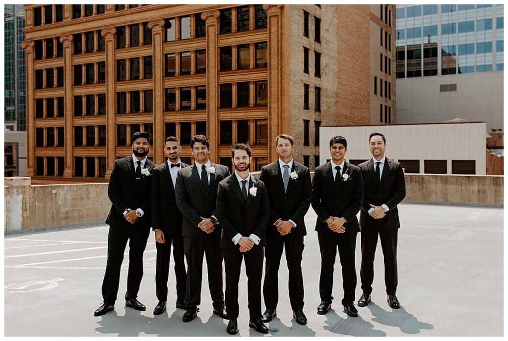 Shane and groomsmen in black suits lined up on the rooftop of the Lumber Exchange Minneapolis
