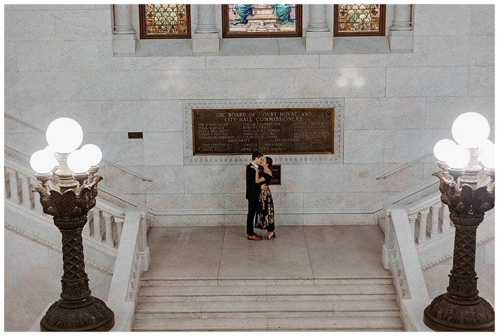 Meredith and Alec standing together on the staircase of Minneapolis City Hall during their engagement session
