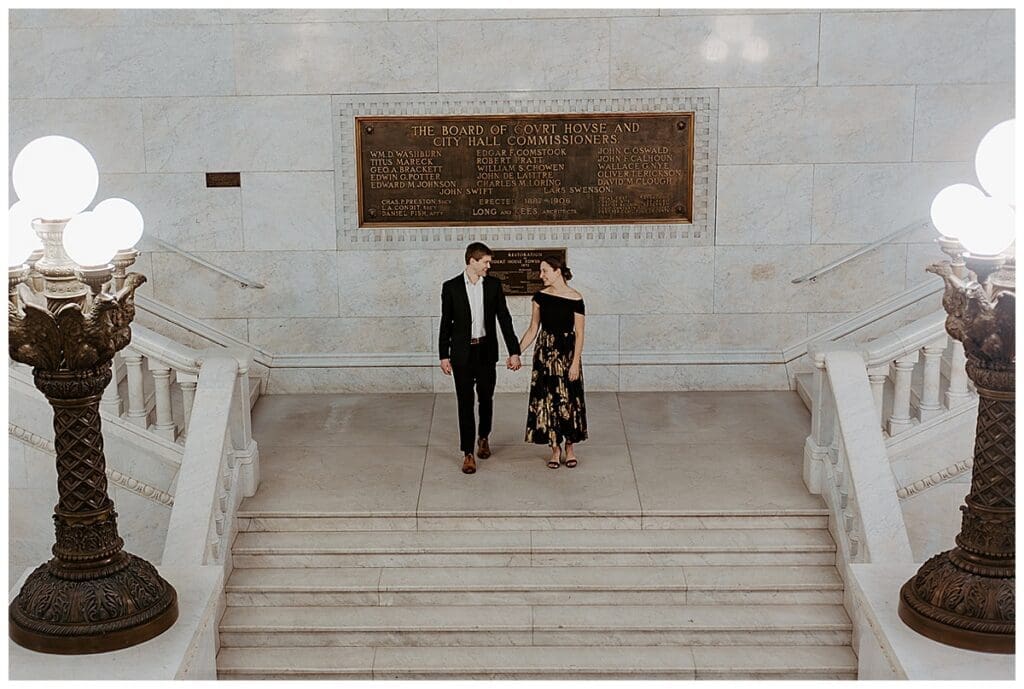 Wide shot of Meredith and Alec walking down the marble staircase at Minneapolis City Hall engagement session