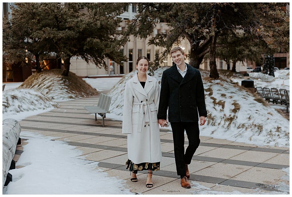 Meredith and Alec walking through a snowy park during their winter engagement session in Minneapolis