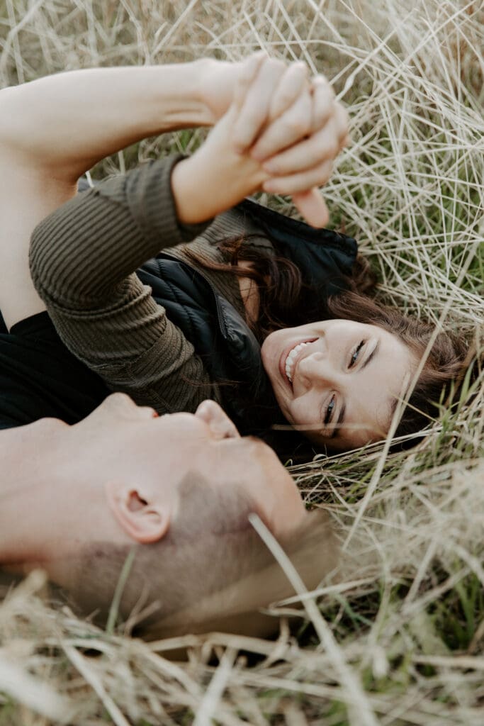 Couple laughing together while lying in tall grass during their engagement session